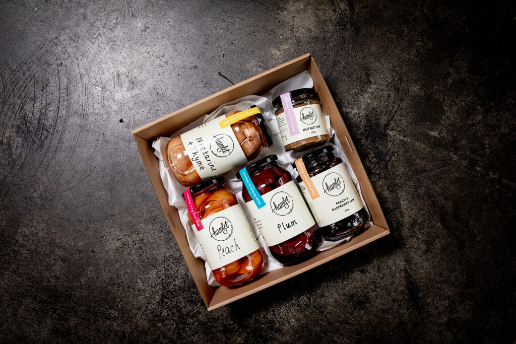A hamper containing jars of Hamlet's Nectarine and Thyme, Plum, and Peach poached fruit preserves, Nut Butter, and Peach and Raspberry Jam.