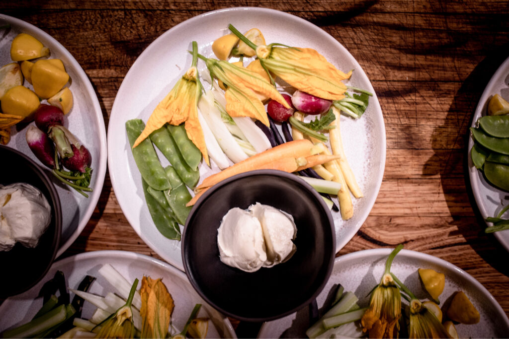 An array of plated vegetables and bowls of dip sitting on a timber table.