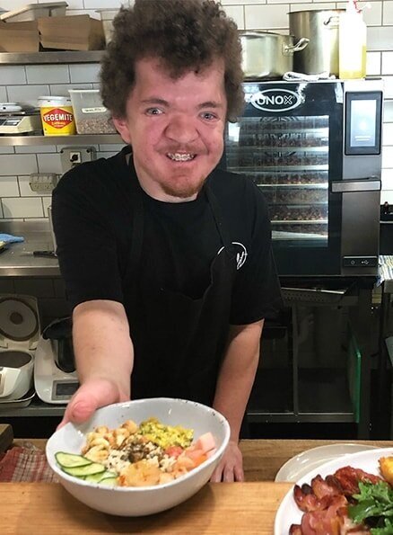 Hamlet's participant Clayton serving a meal and smiling for a photo.