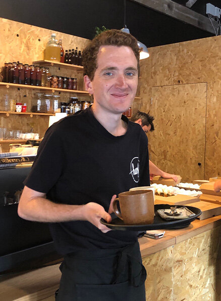 Hamlet's participant James carrying an order to a table and smiling for a photo.