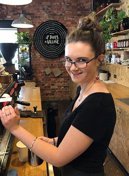 Hamlet's participant Sophie smiling for a photo standing at the coffee machine frothing milk.