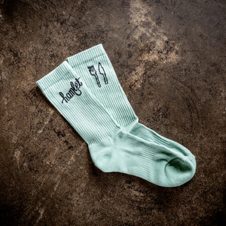 A pair of pale green socks embroidered with the Hamlet logo at the top of the ankle cuff.
