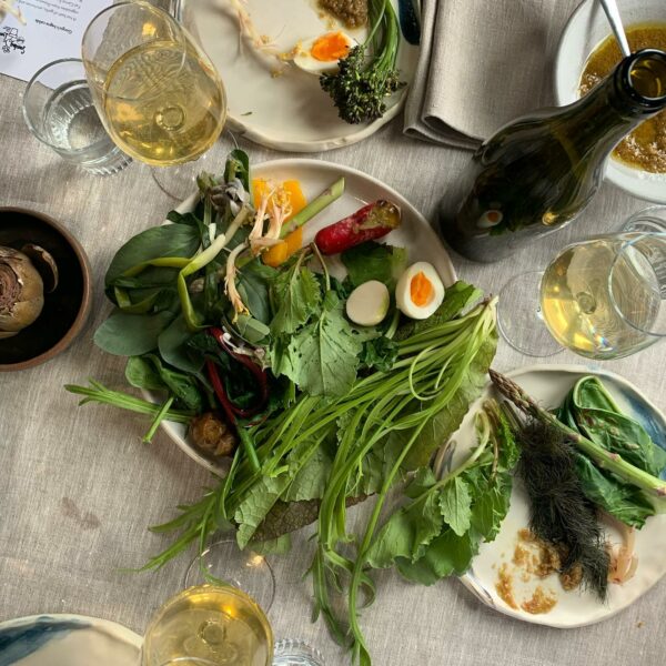 Three plates of vegetables, besides a wine bottle, three wine glasses and two glasses of water.