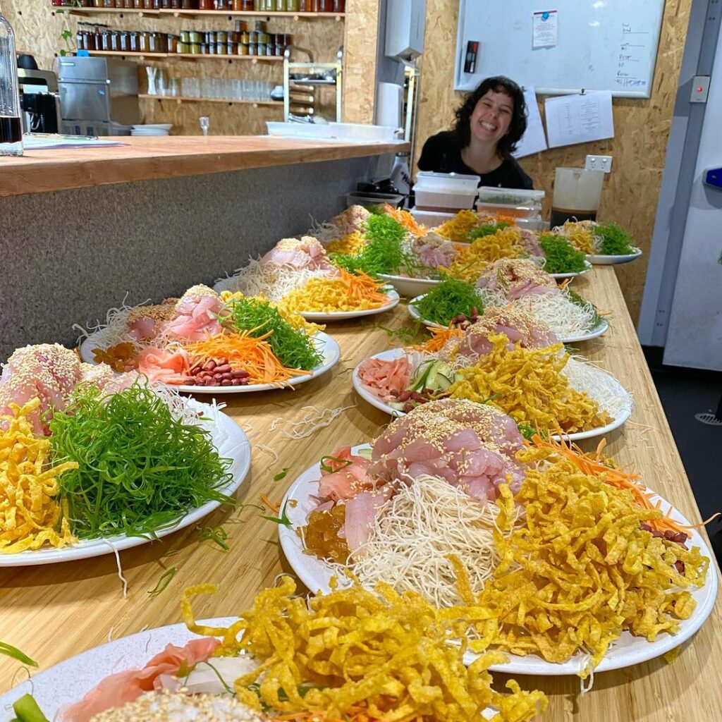 One of Hamlet's participants smiling and standing at the end of the kitchen bench that has multiple plates of food sitting on top.