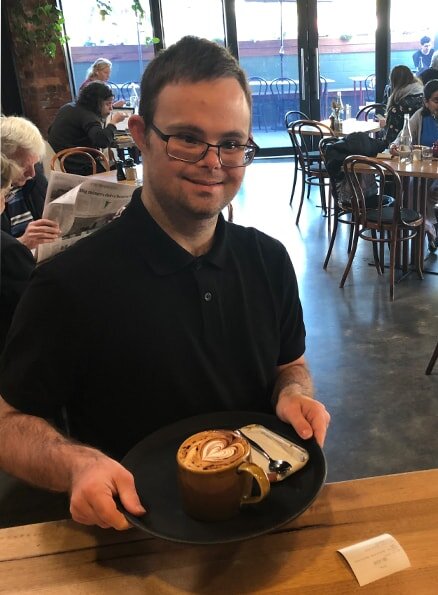 Hamlet's participant Daniel standing at the counter wearing a black shirt and holding a cup of coffee.