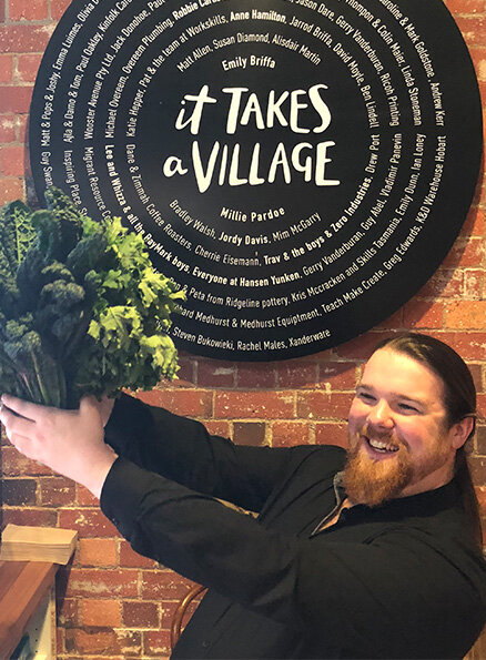 Hamlet's participant Declan is smiling for a photo wearing a black shirt holding a large bunch of kale and salad leaves.