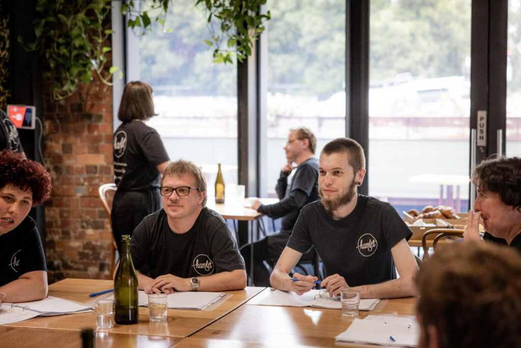 Group of Hamlet participants sitting at the table wearing black Hamlet T-shirts.