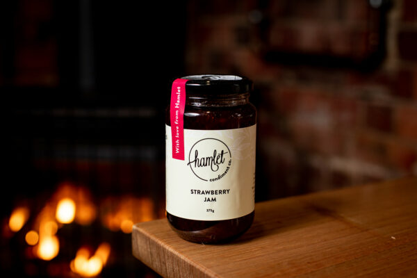 A jar of Hamlet's Strawberry Jam sitting on a timber table.