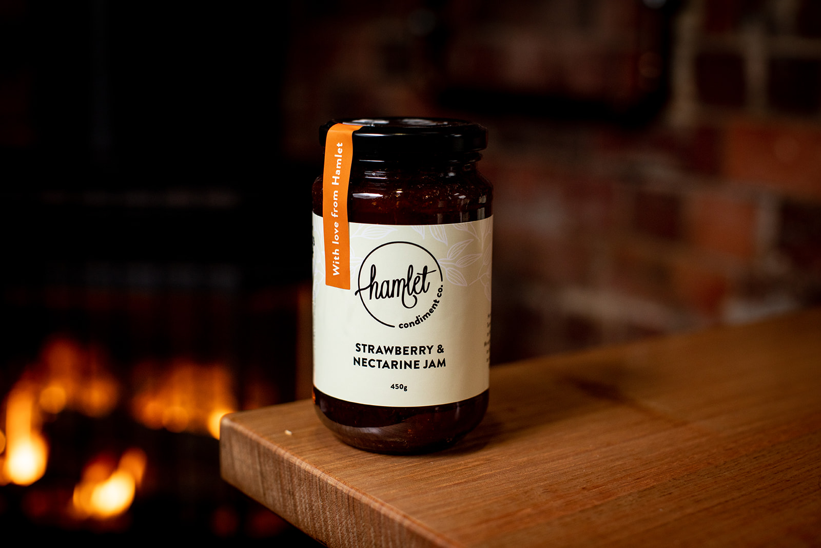 A jar of Hamlet's Strawberry and Nectarine Jam sitting on a timber table.