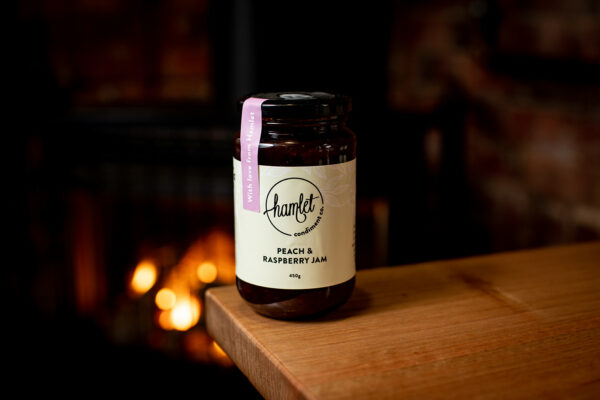 A jar of Hamlet's Peach and Raspberry Jam sitting on a timber table.