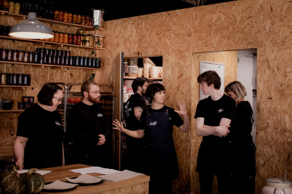 Group of Hamlet's participants standing in the cafe talking amongst each other wearing black Hamlet t-shirts.