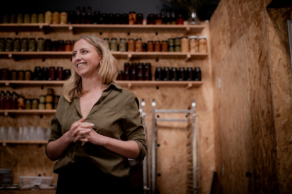 Hamlet's co-founder and CEO Emily is smiling looking to the right with her hands folded, wearing a khaki shirt.