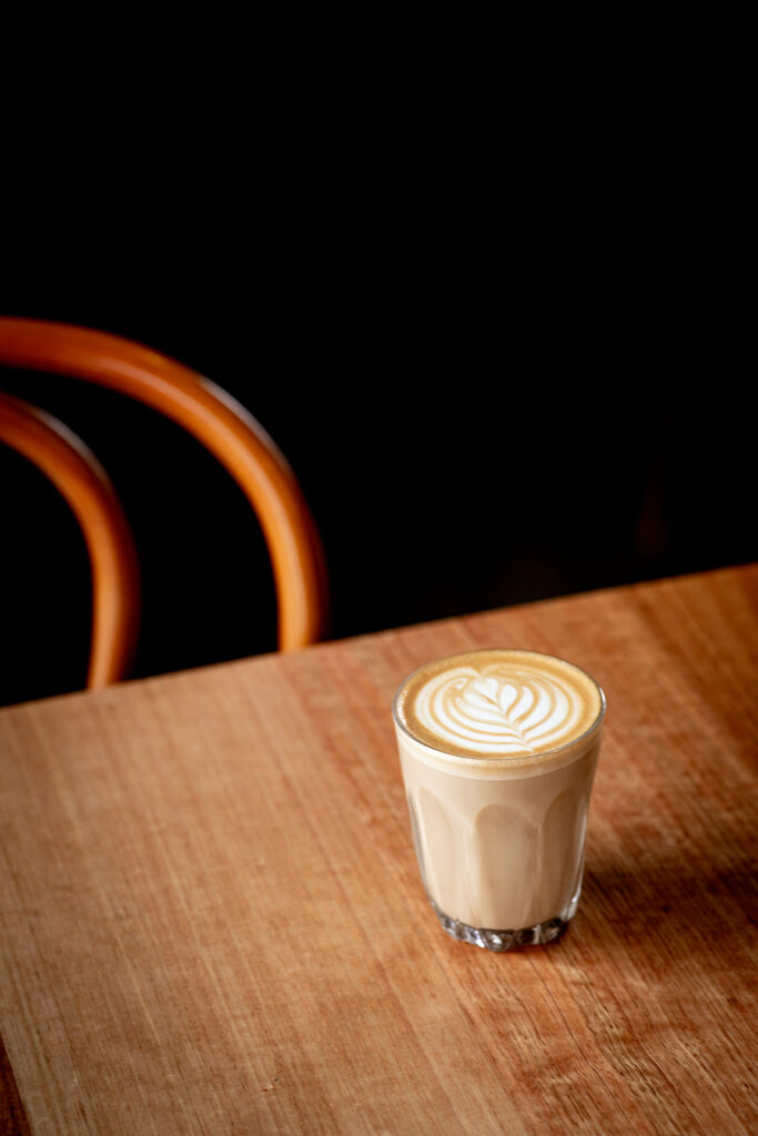 Small cup of coffee with swirl of frothed milk sitting on a timber table.