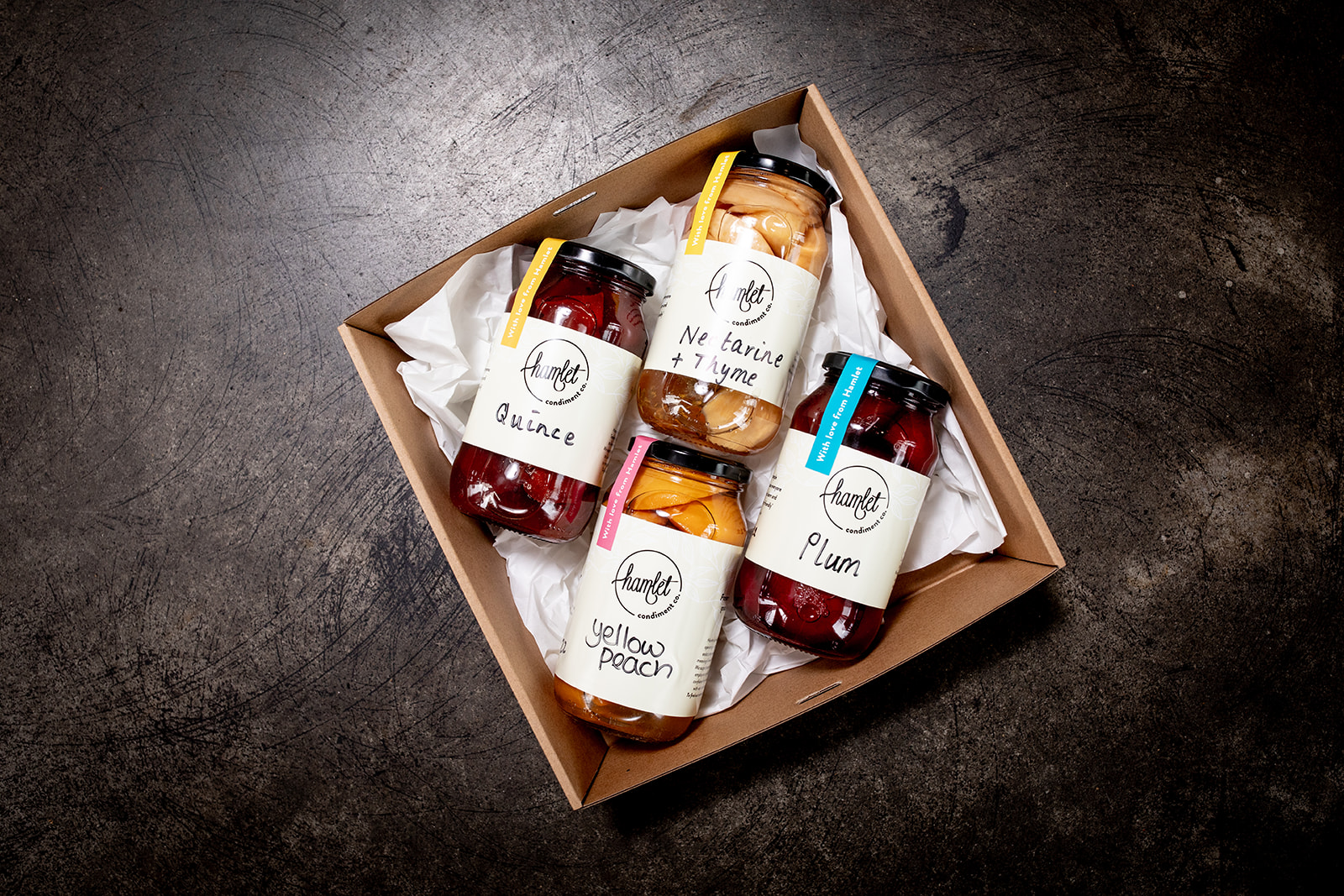 A hamper containing jars of Hamlet's Quince, Nectarine and Thyme, Plum, and Yellow Peach poached fruit preserves.