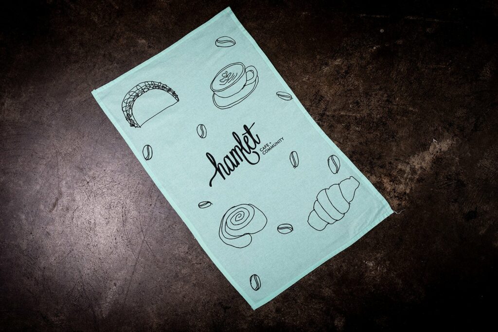 A Hamlet tea towel sitting on a concrete bench with artwork by their work experience participants.